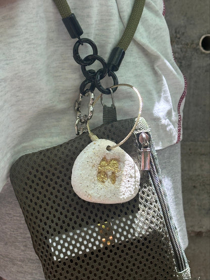 Close-up of a keychain with a textured round tag and heart-shaped charm on a white fabric background.