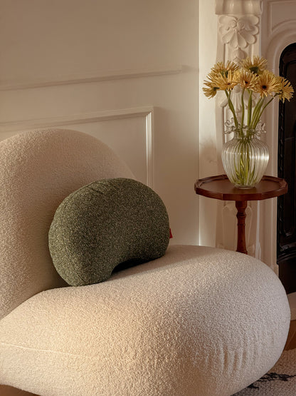 White textured armchair with a green cushion next to a small wooden table with a vase of yellow flowers.