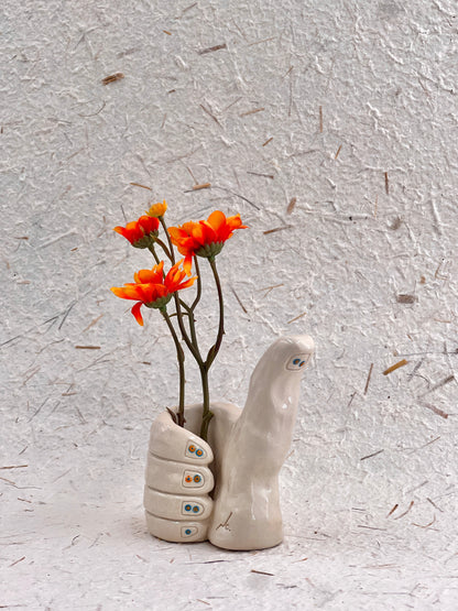 Ceramic hand-shaped vase with orange flowers on a textured gray background