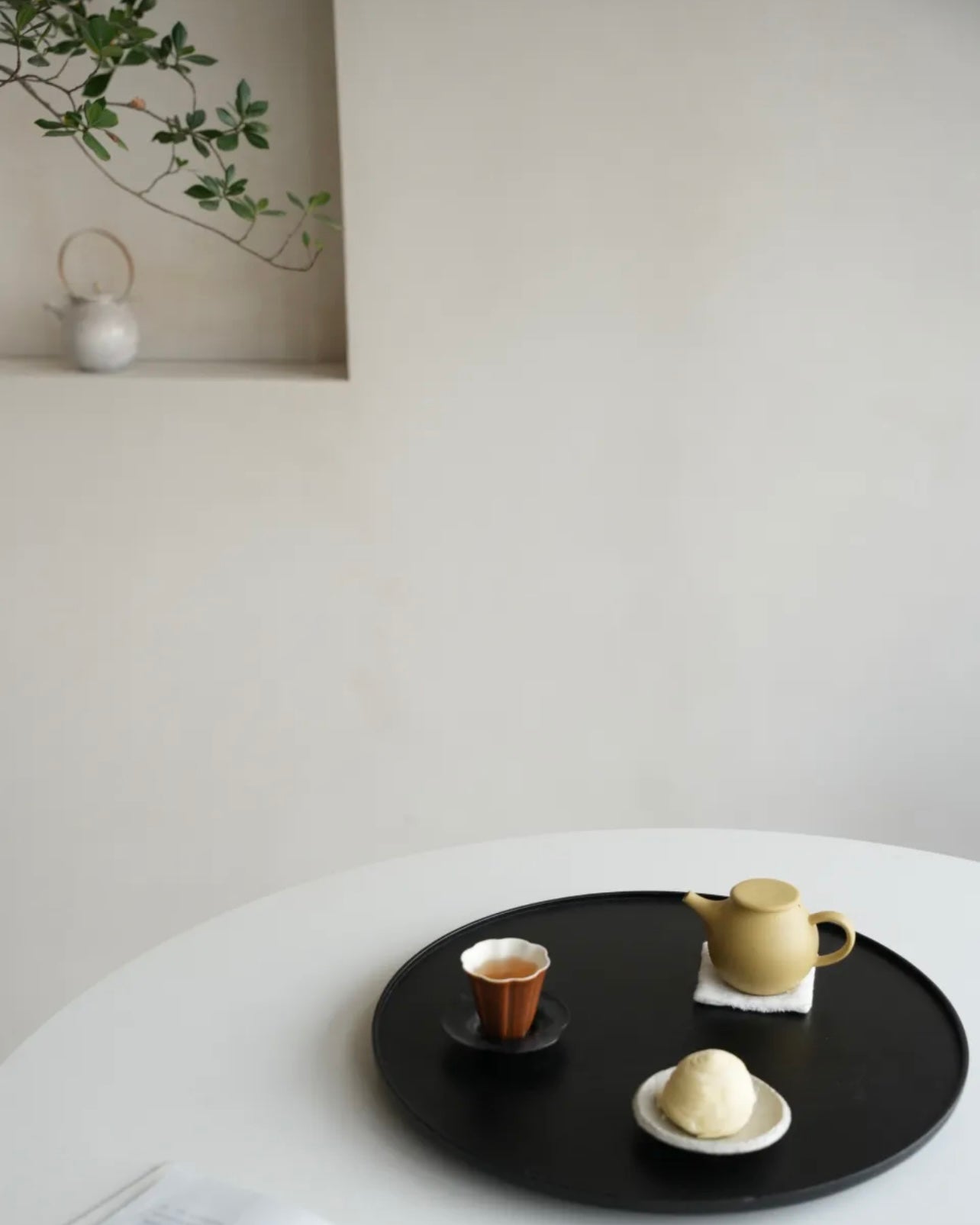 Tea set on a black tray with a white wall and plant in the background