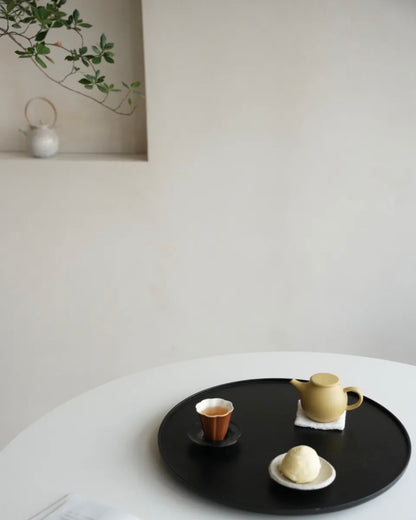 Tea set on a black tray with a white wall and plant in the background