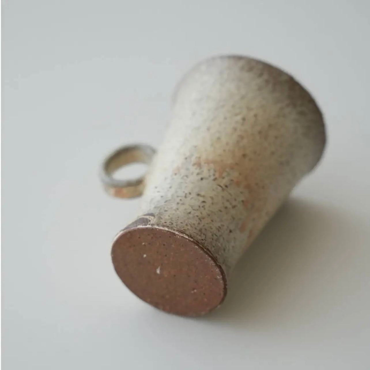 Cylindrical ceramic object with a textured surface on a light gray background