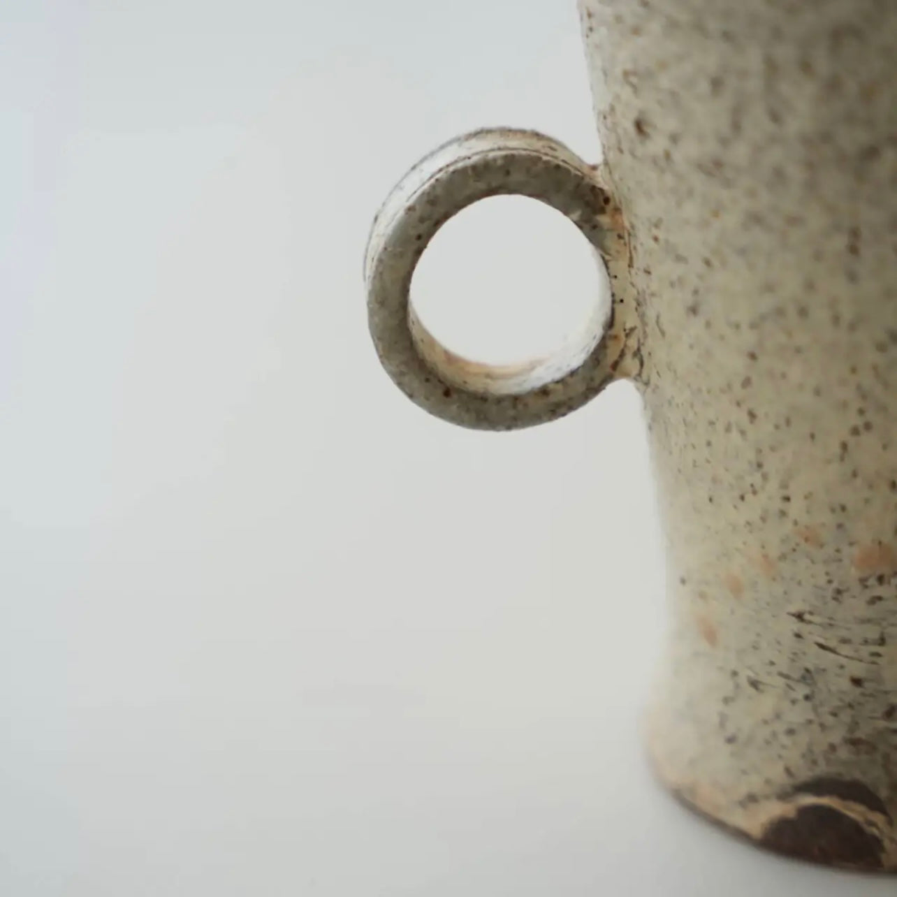 Close-up of a ceramic mug with a speckled texture on a light gray background