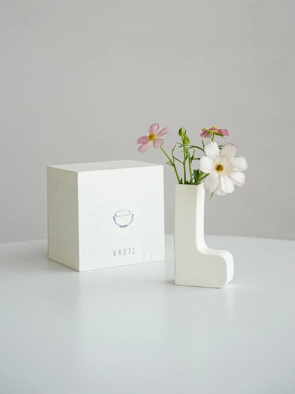 White vase with flowers on a gray surface and light gray background