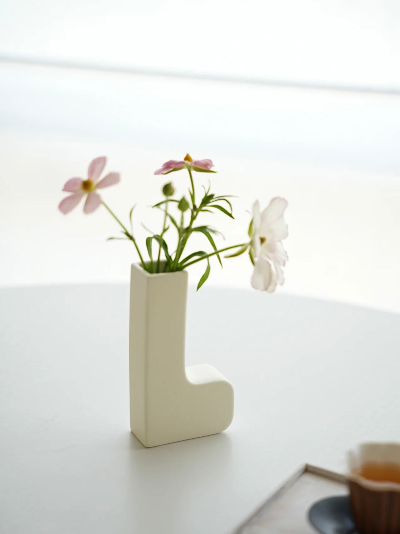 White letter 'L' vase with flowers on a light surface