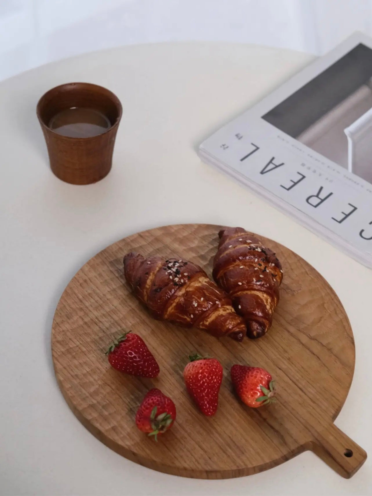 Wooden cutting board with croissants and strawberries on a white surface.