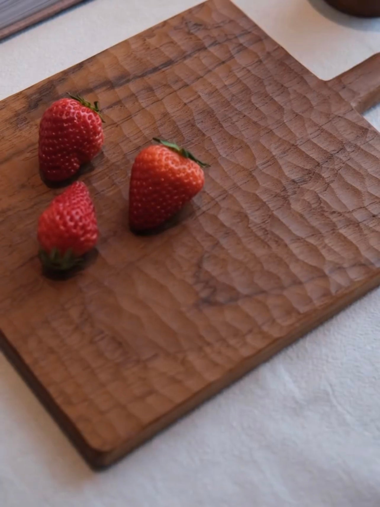 Three strawberries on a wooden cutting board