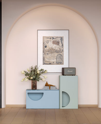 Decorative setup with a framed picture, vase, and small table against a light pink wall.