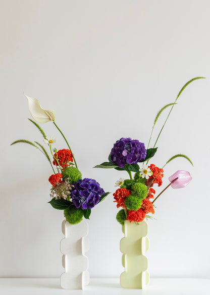 Two floral arrangements in white vases on a light background