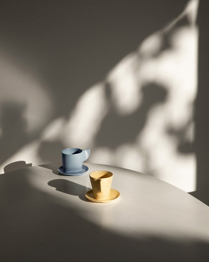 Two ceramic cups, one blue and one yellow, on a white surface with soft shadows.